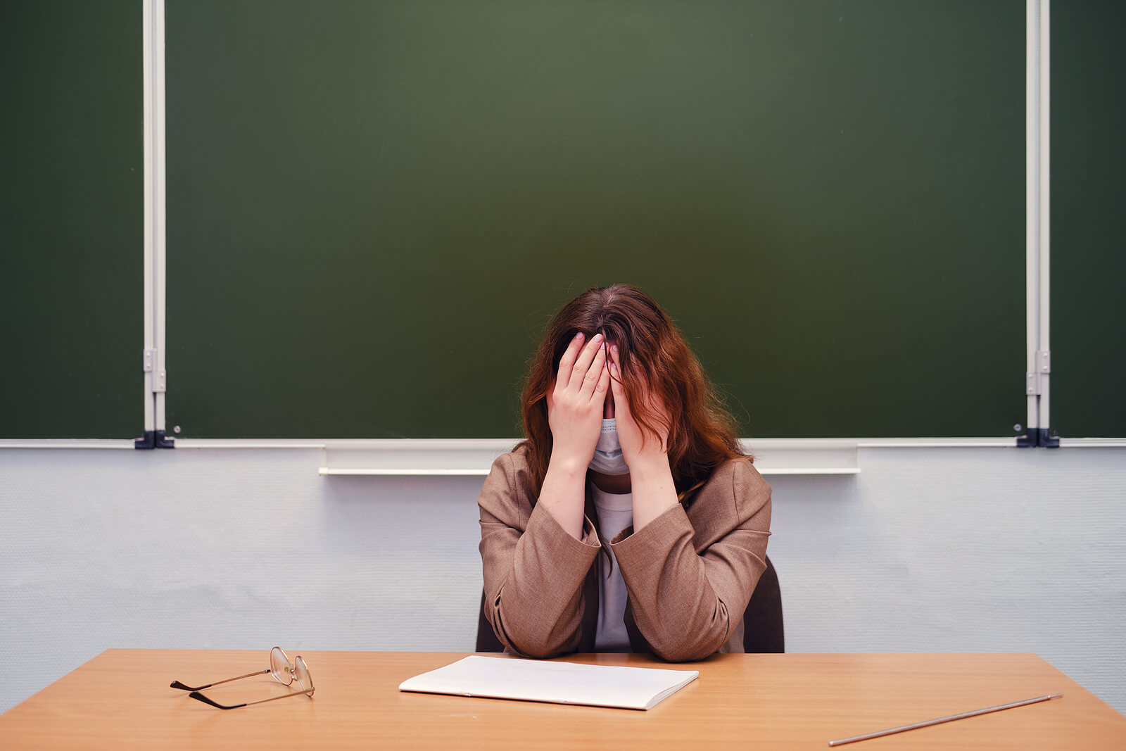 Profesora llorando en la mesa de clase porque sufre bullying.