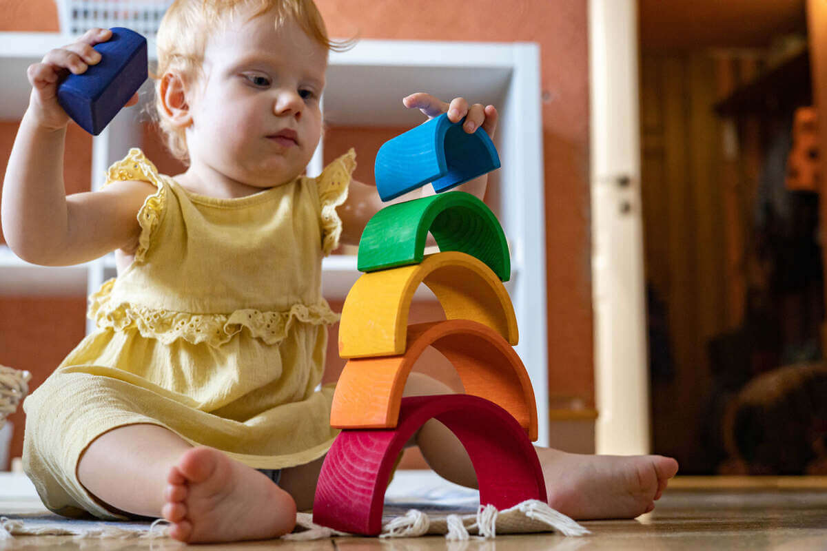 Niña juega con un juguete Montessori de arcoíris en madera 