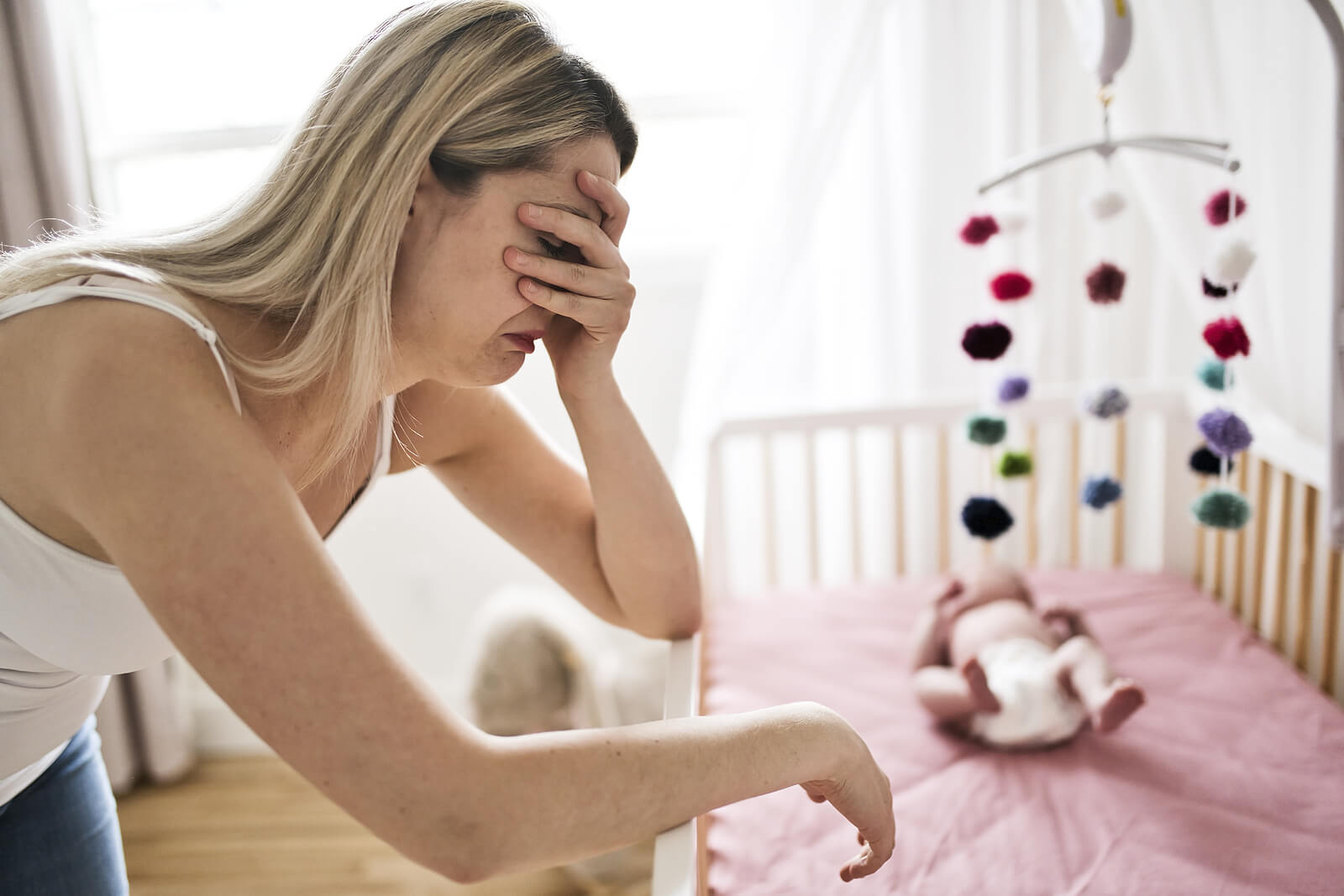 A mother with postpartum depression crying by her baby's crib.
