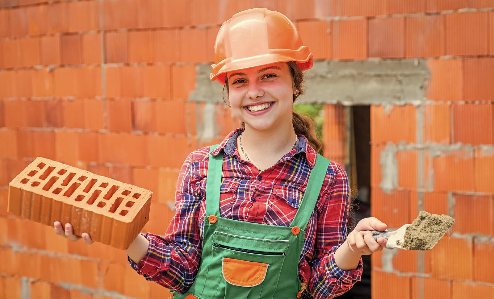 A teenage girl helping to build a brick wall.