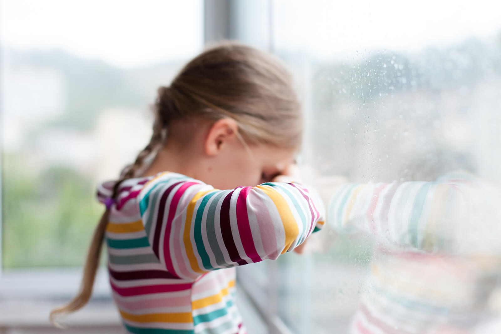 Niña con pluviofobia mirando la lluvia a través de la ventana.