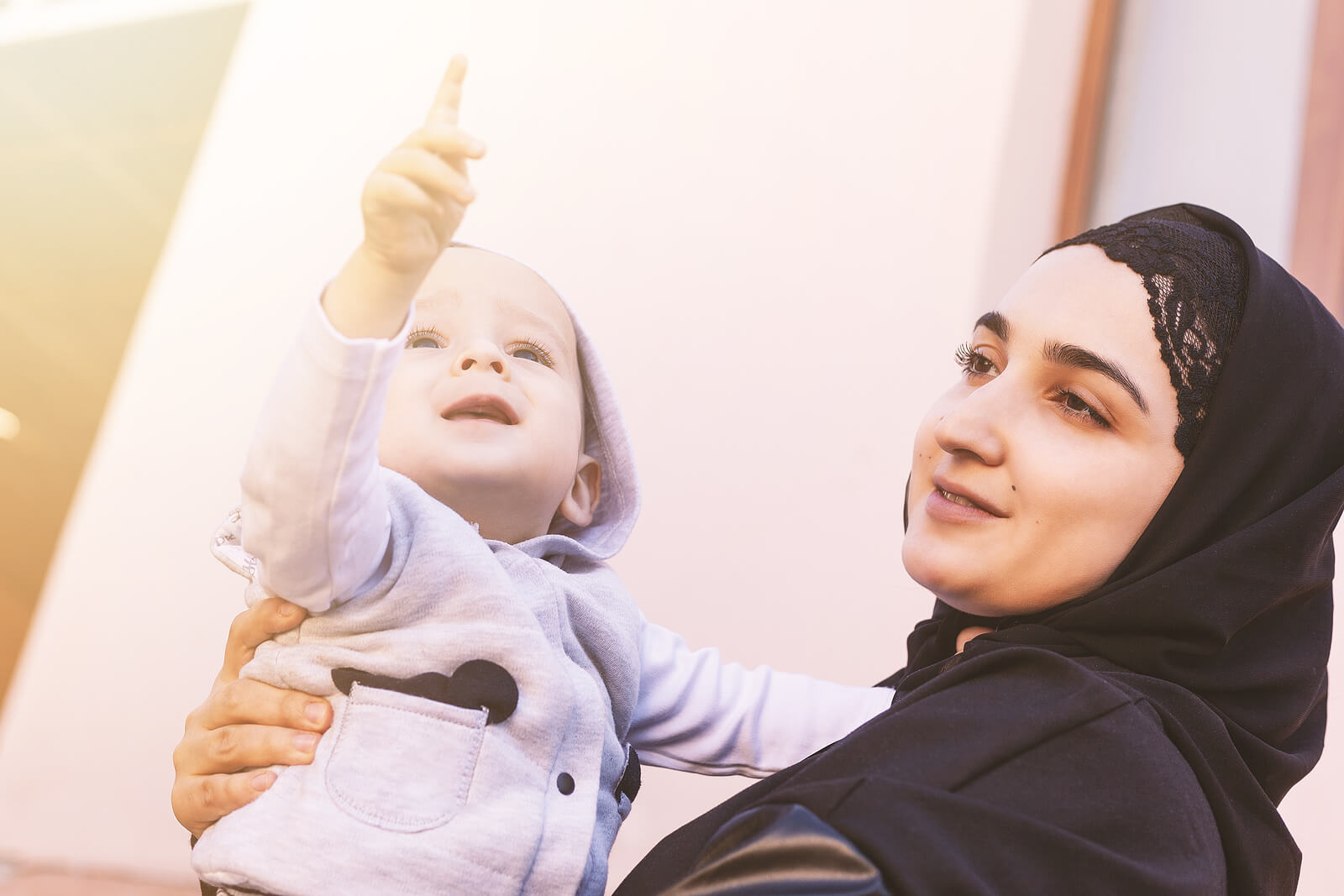 A Middle-eastern woman holding a baby boy who's pointing to the sky.