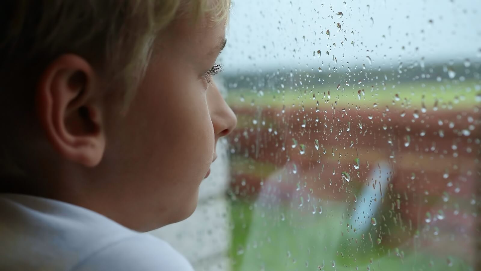 Niño mirando por la ventana pensado en el suicidio.
