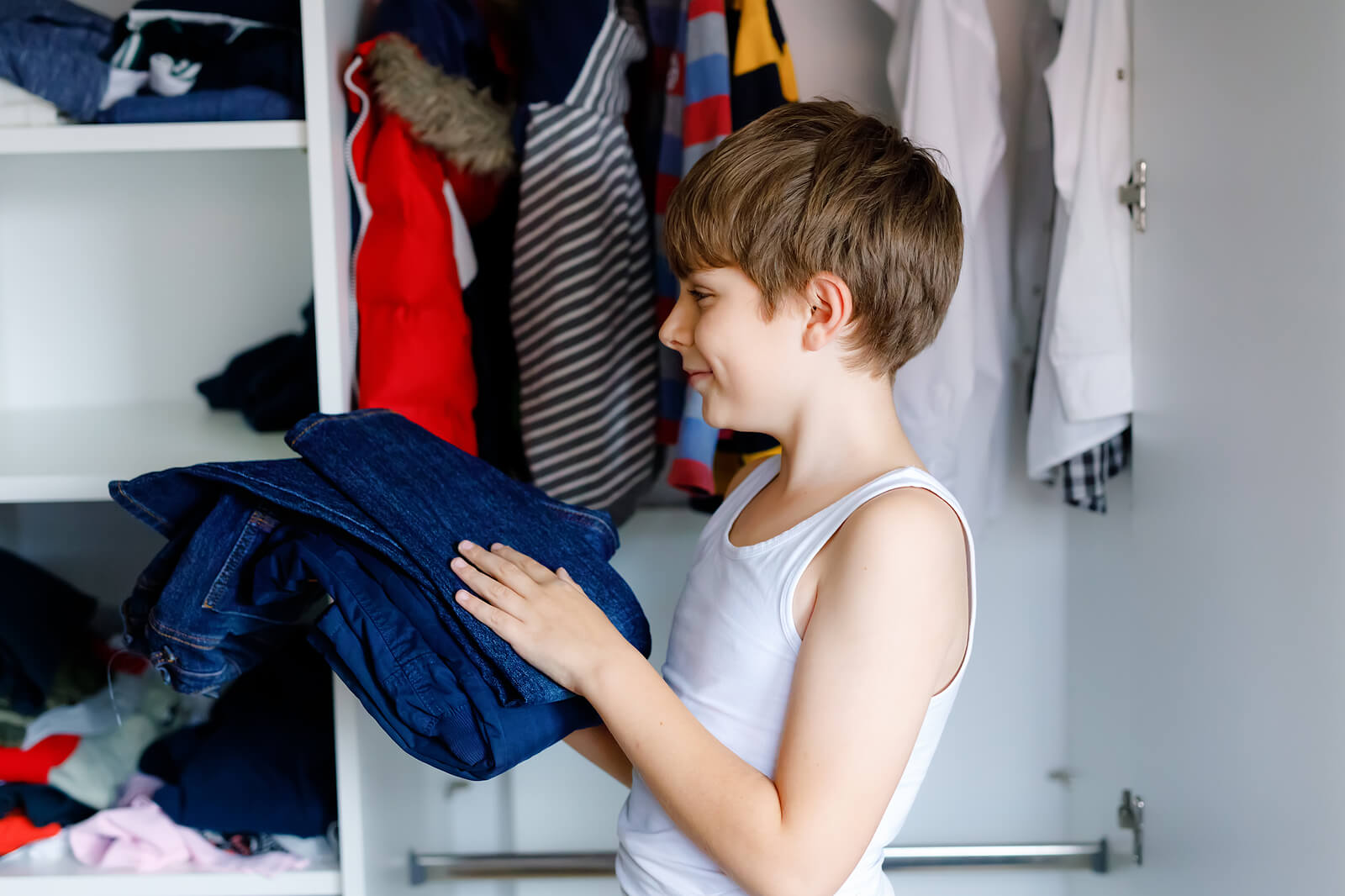 A preteen boy folding and putting away a pair of jeans.