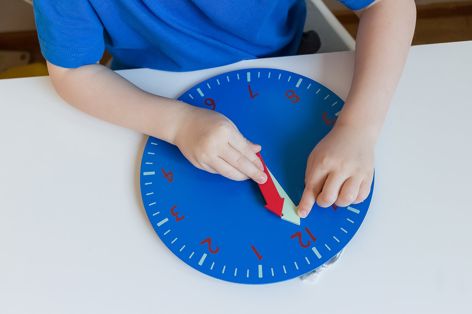 Niño aprendiendo la hora haciendo manualidades con un reloj.