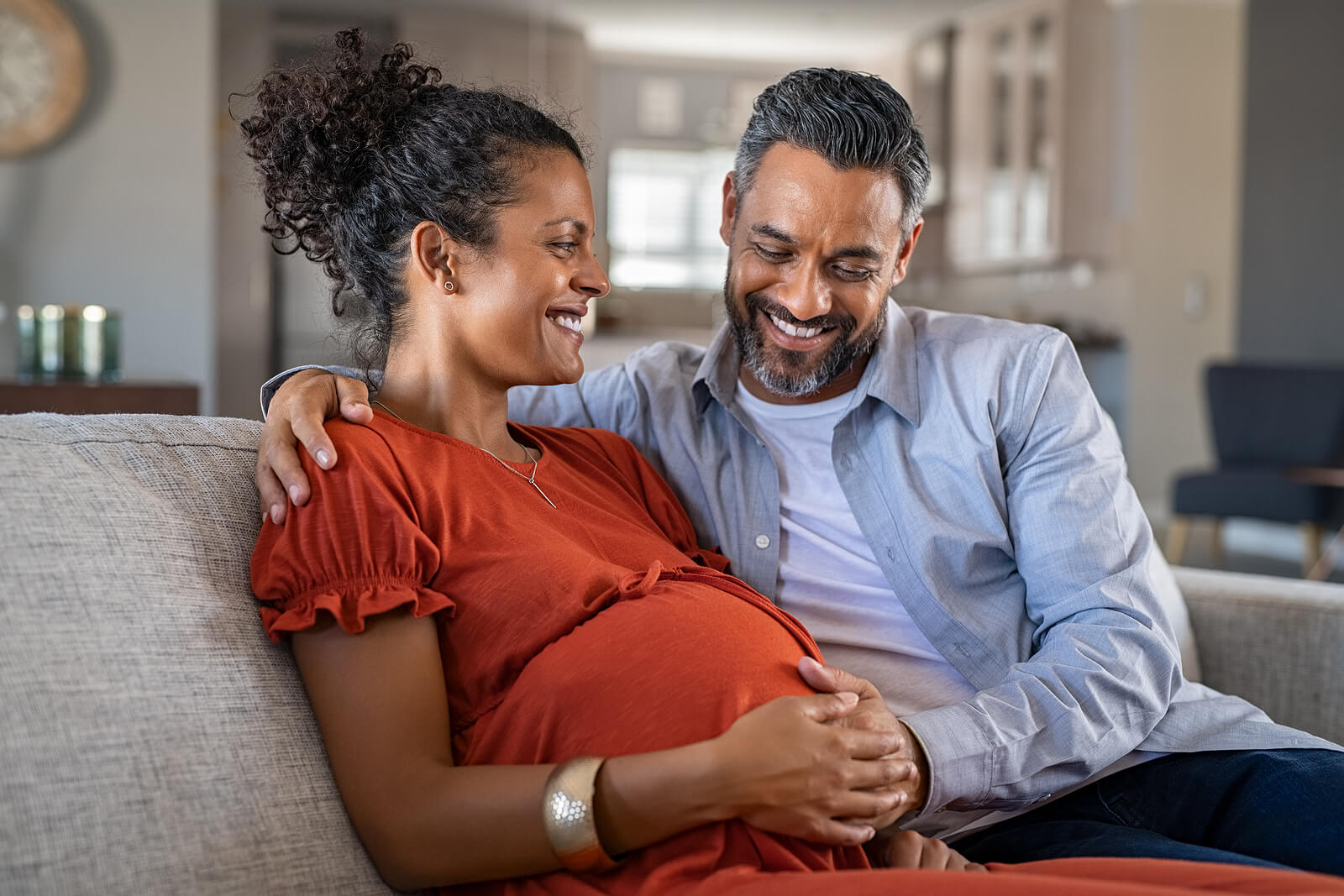 A smiling man and woman with their hands on the woman's pregnant belly.
