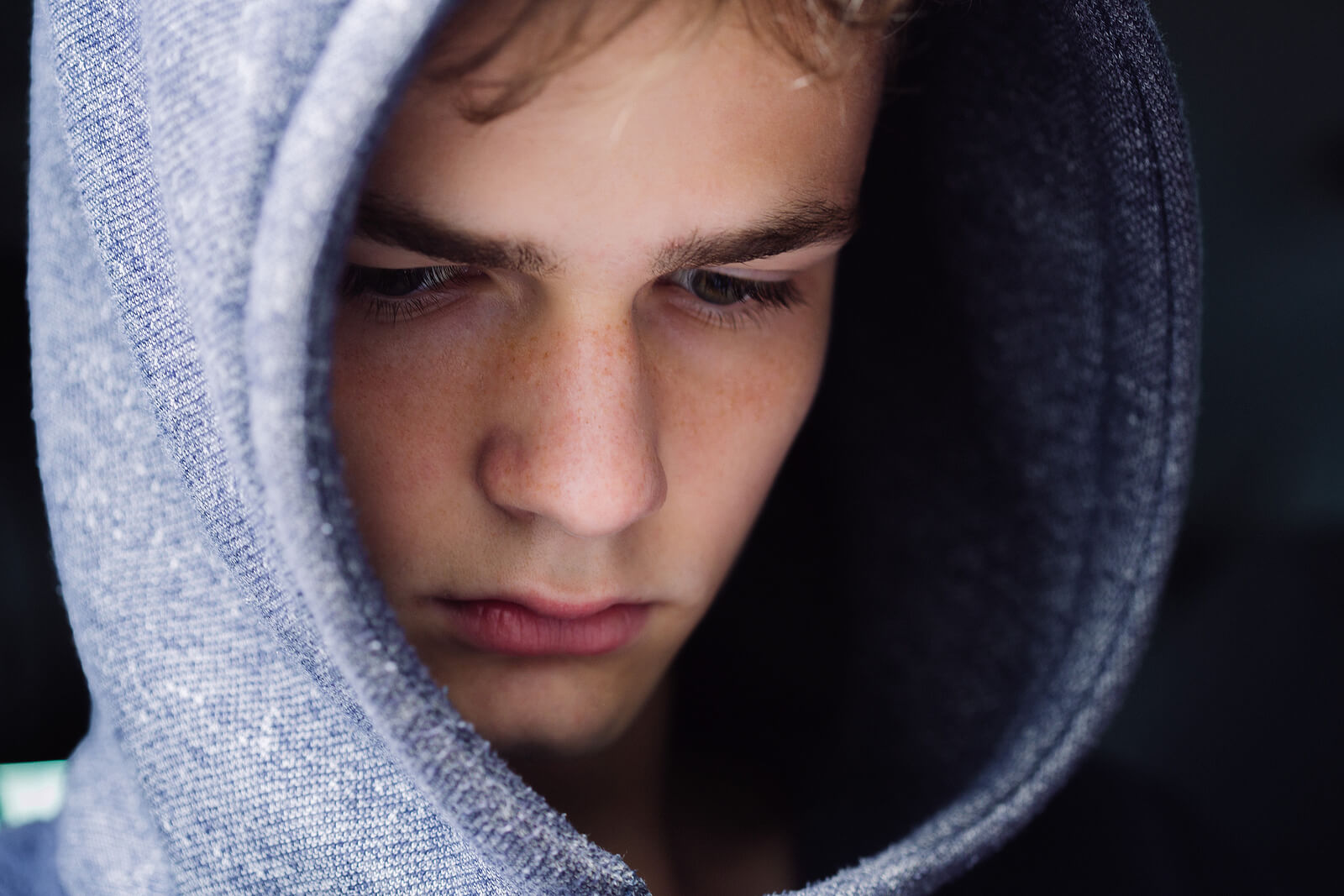A teen boy wearing a hoodie and looking sad.