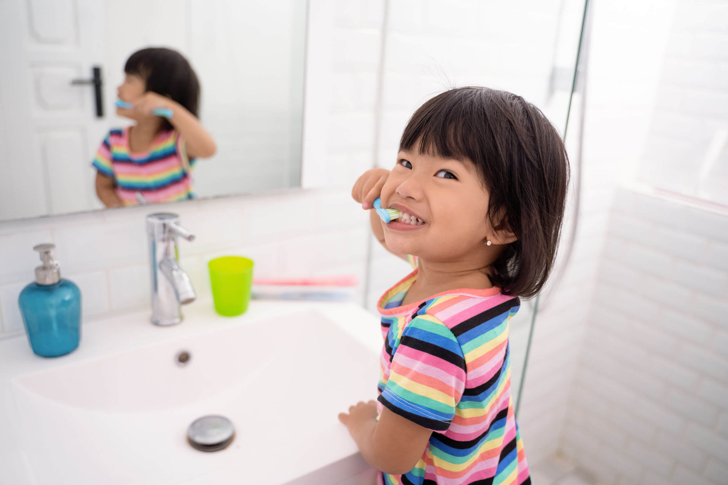 A toddler girl brushing her teeth by the sink.