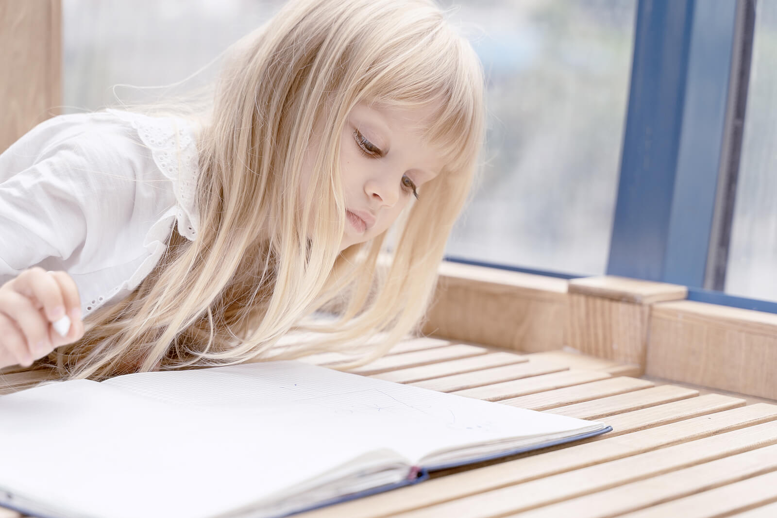 Niña pensando en la escritura a mano mientras observa un cuaderno.