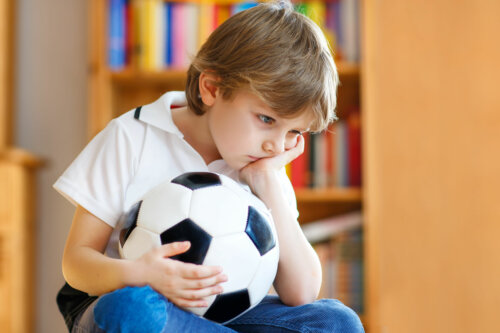 Niño con un balón de fútbol triste debido a su negatividad.