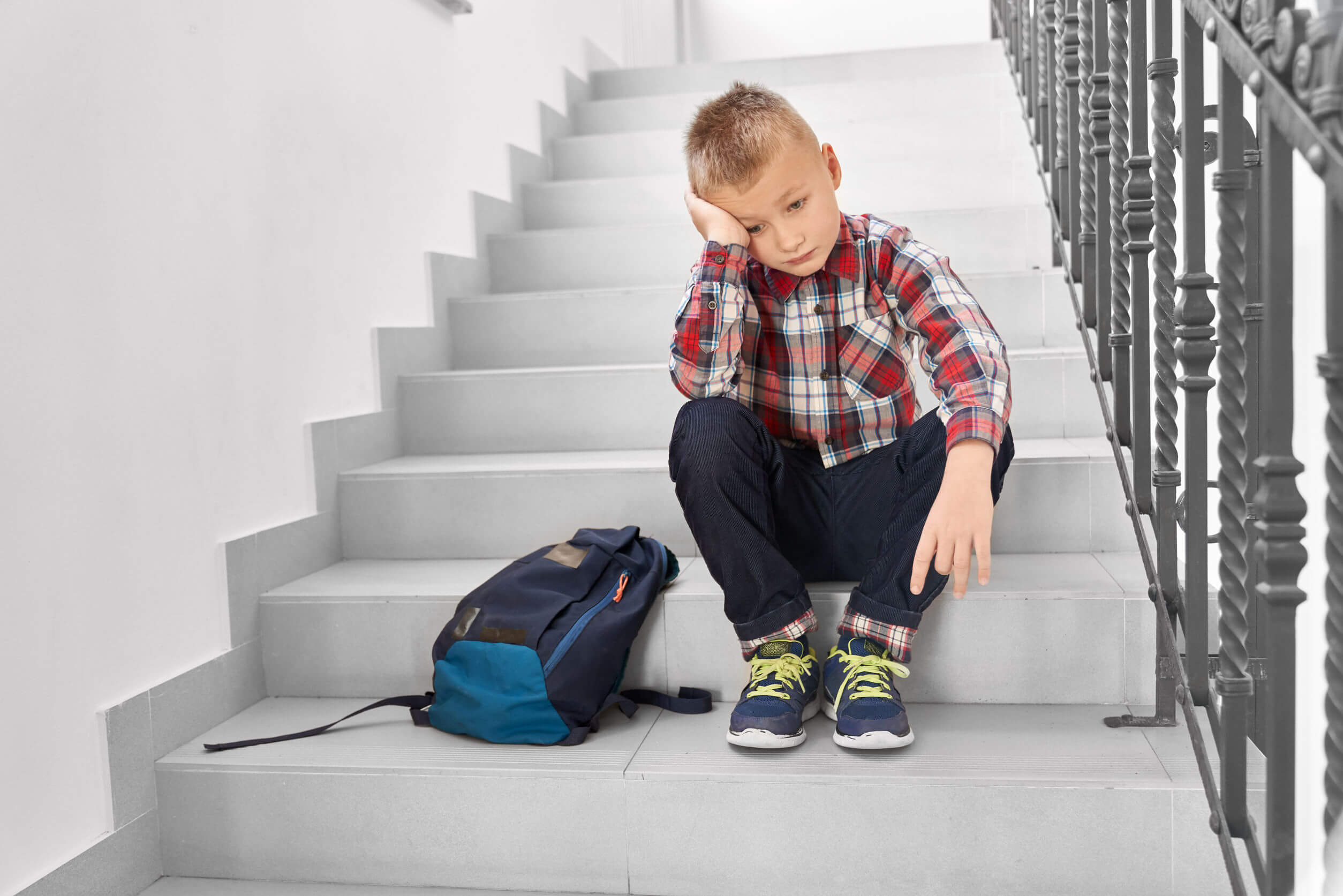 Niño sentado en las escalera del colegio sin motivación para estudiar.