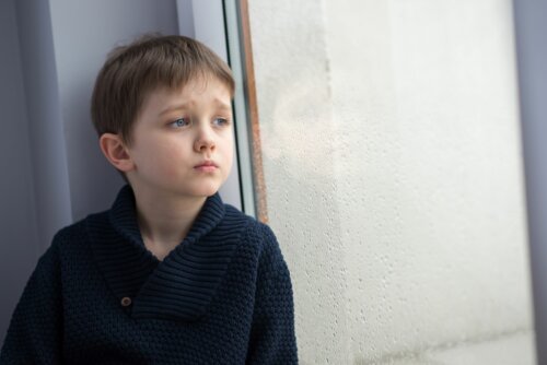 Niño mirando por la ventana porque se siente solo.