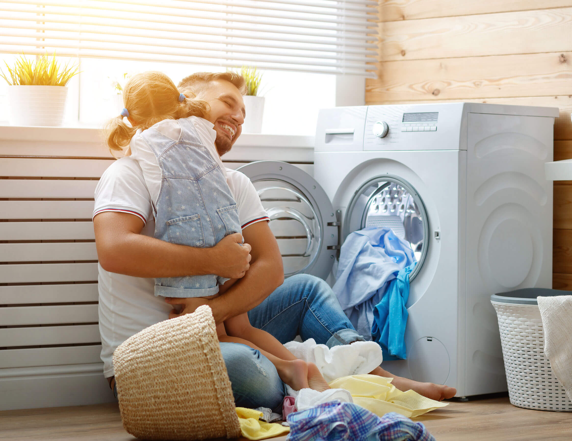 Un père qui s'occupe du linge de la maison avec sa fille dans les bras.