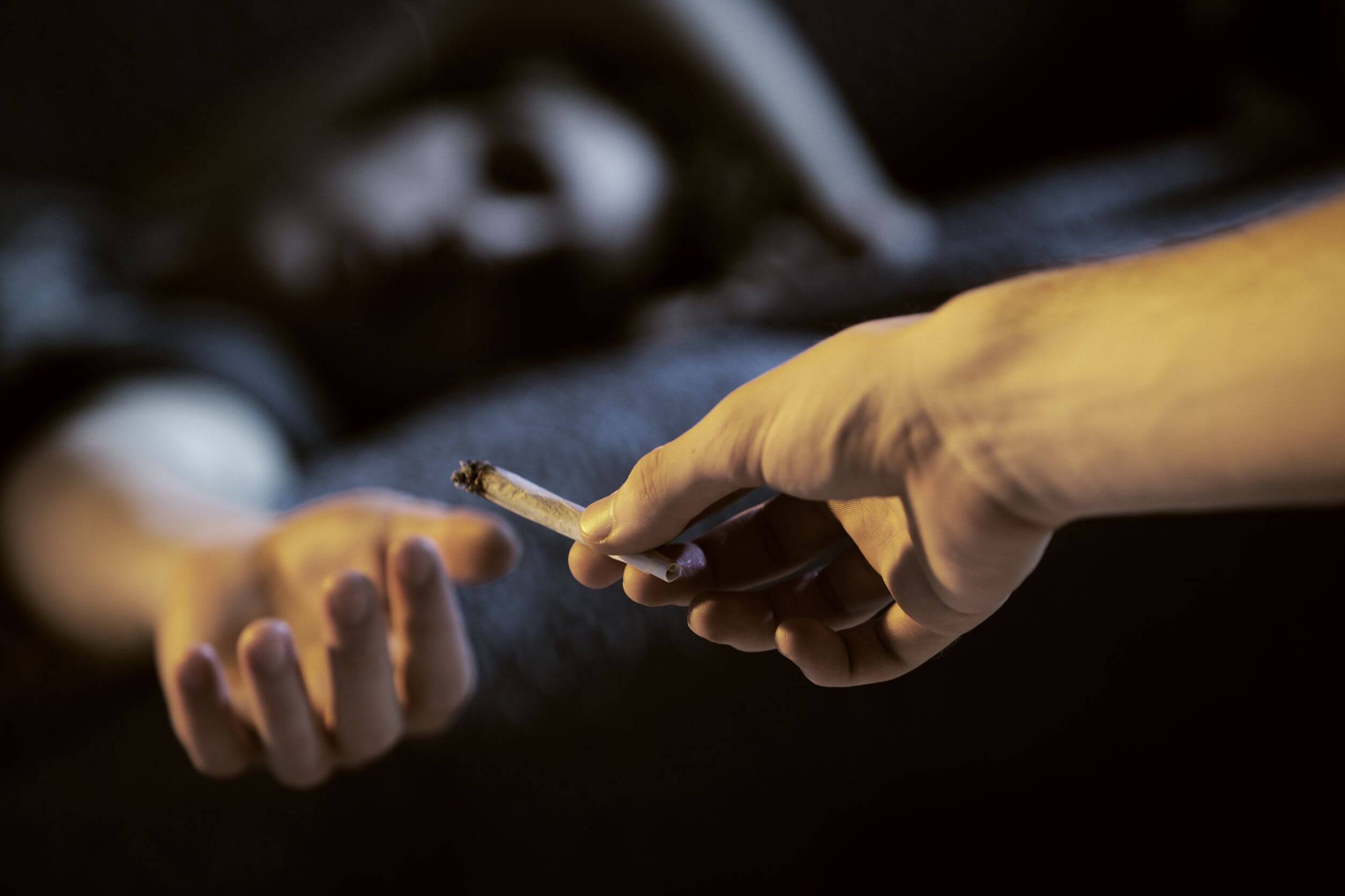 A person handing a joint to another person that's lying on a couch.