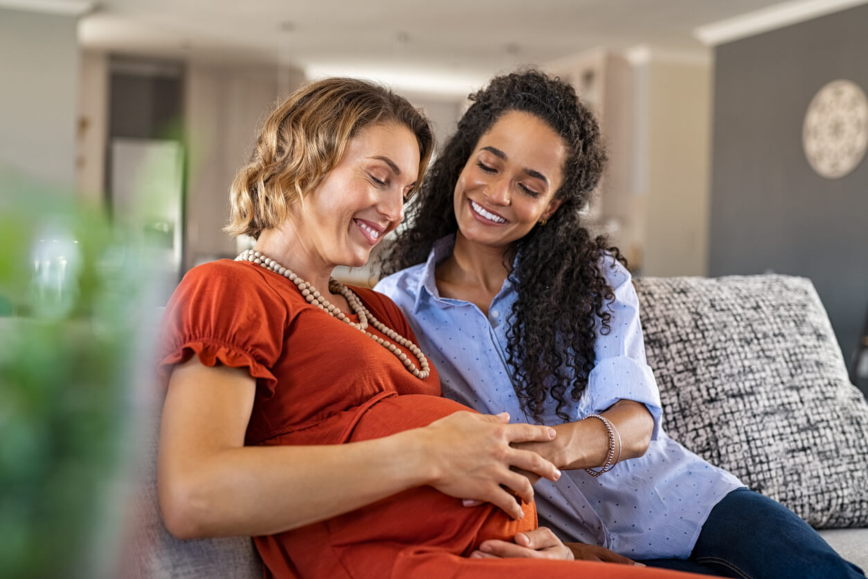 Une femme enceinte et son amie qui touche son ventre et les mouvements du bébé. 