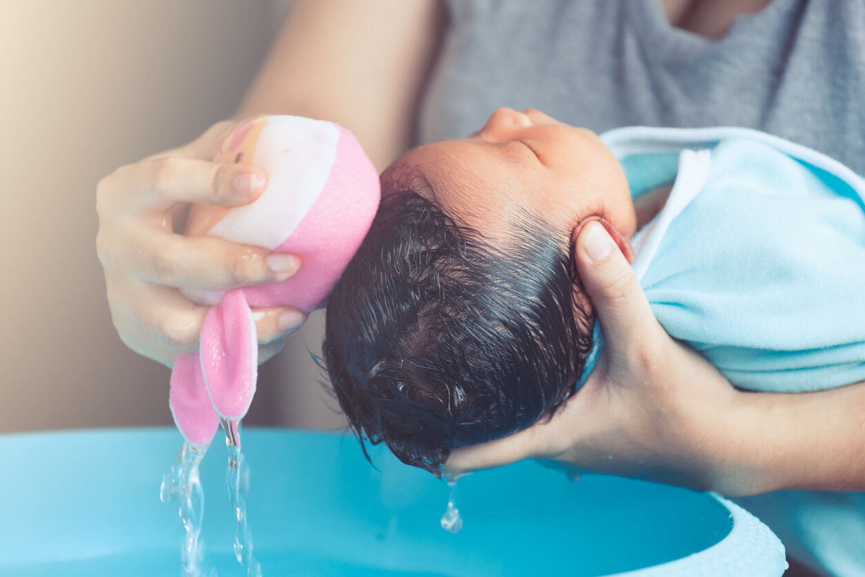 A parent washing a newborn baby's hair over a basin.