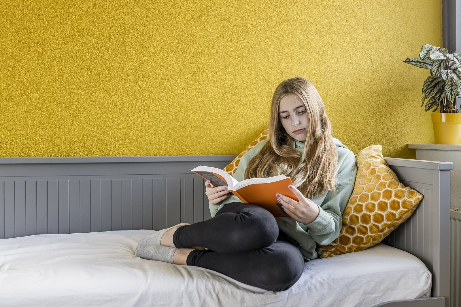 A teenager sitting on a daybed, hooked on reading.