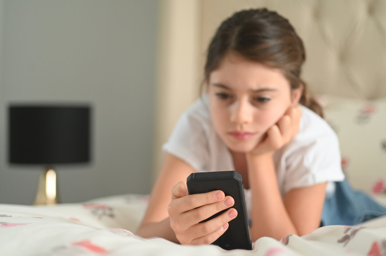 Niña mirando el teléfono móvil sufriendo estrés digital.