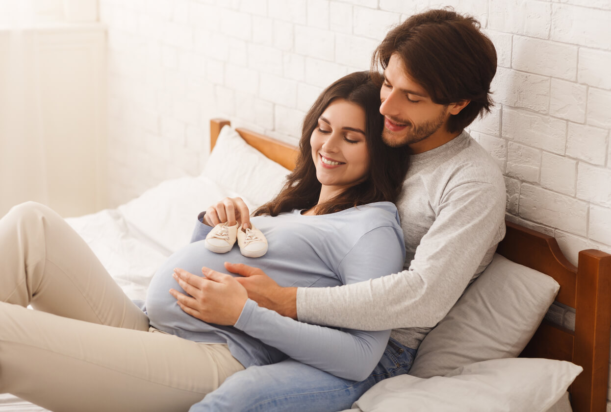 Framtida föräldrar ligger i sängen och tittar på babyskor.