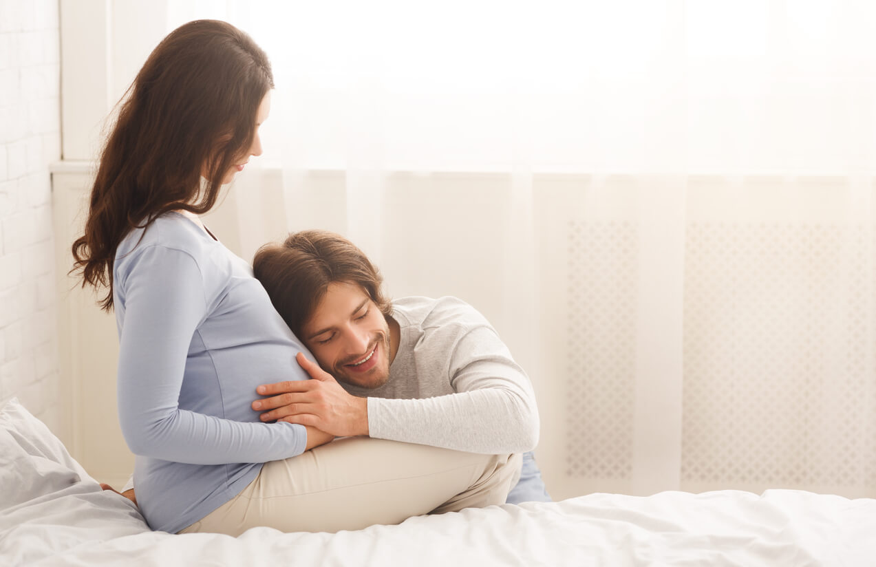 Futuro padre escuchando en la barriga de su mujer embarazada.