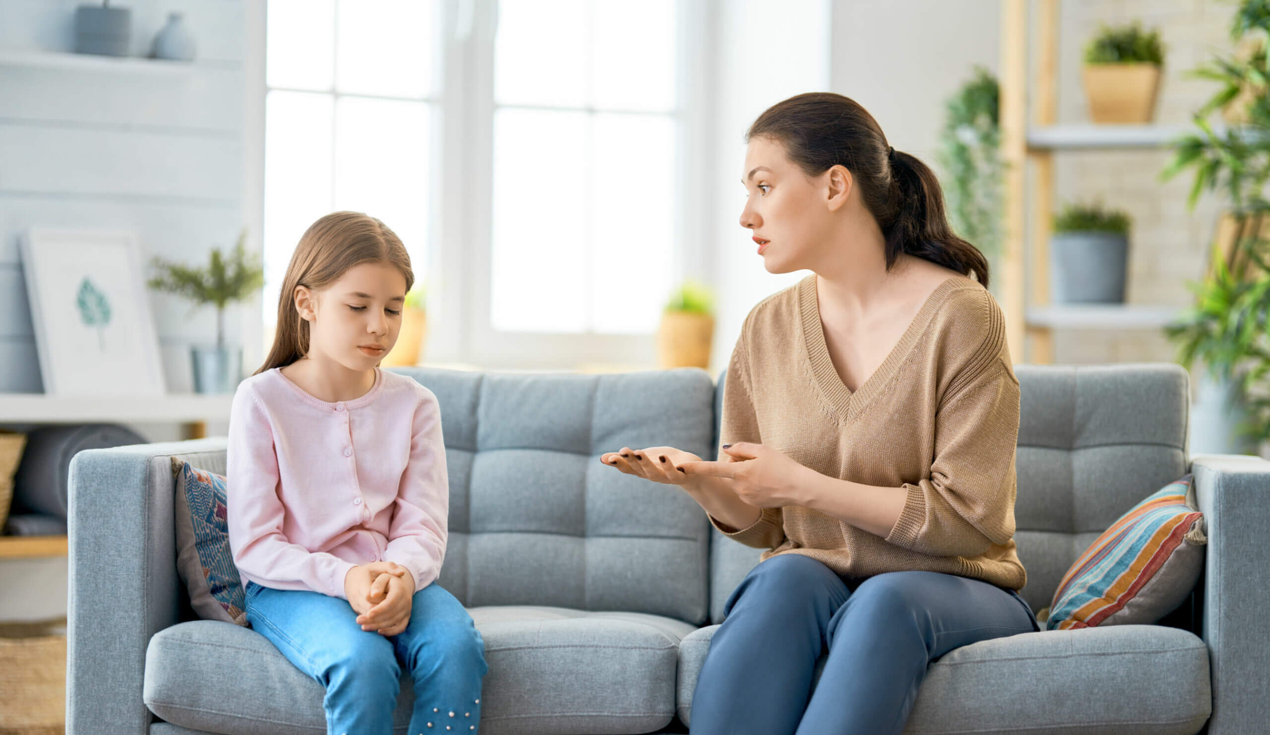 A mother and her young daughter having a serious conversation on the couch.