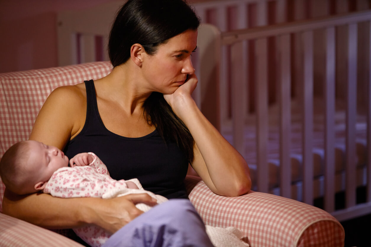 A woman holding her newborn in an armchair, looking off into the distance.