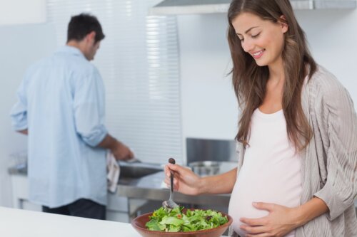 Mujer cocinando con verduras de hoja verde durante el embarazo.