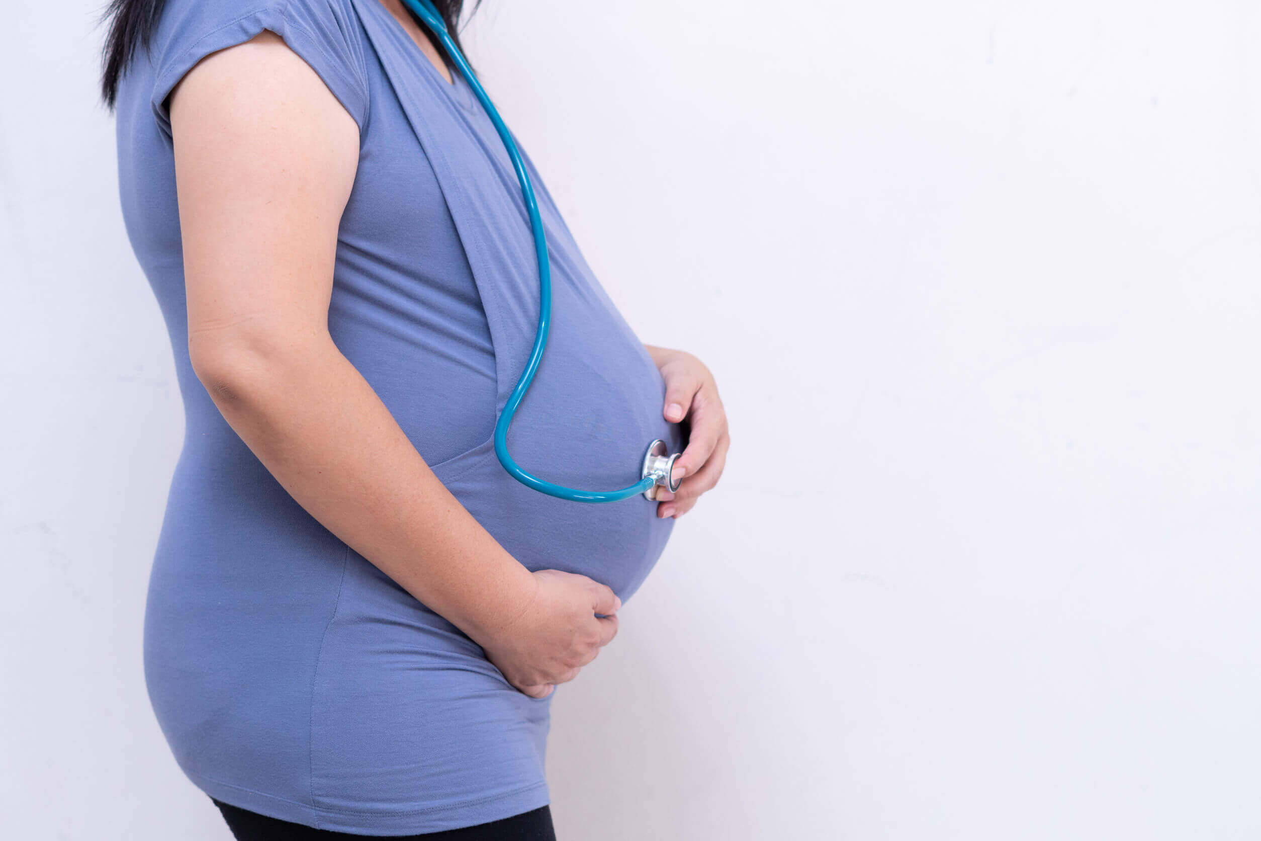 A pregnant woman holding a stethoscope to her belly.