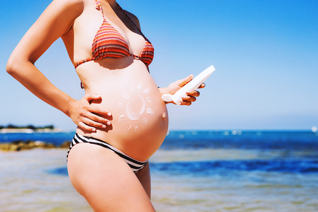 Femme enceinte sur la plage appliquant un écran solaire pour traiter la peau sèche pendant la grossesse.