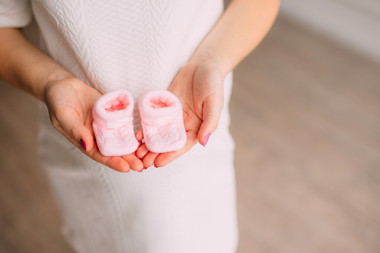 Femme enceinte avec des chaussons roses dans ses mains.