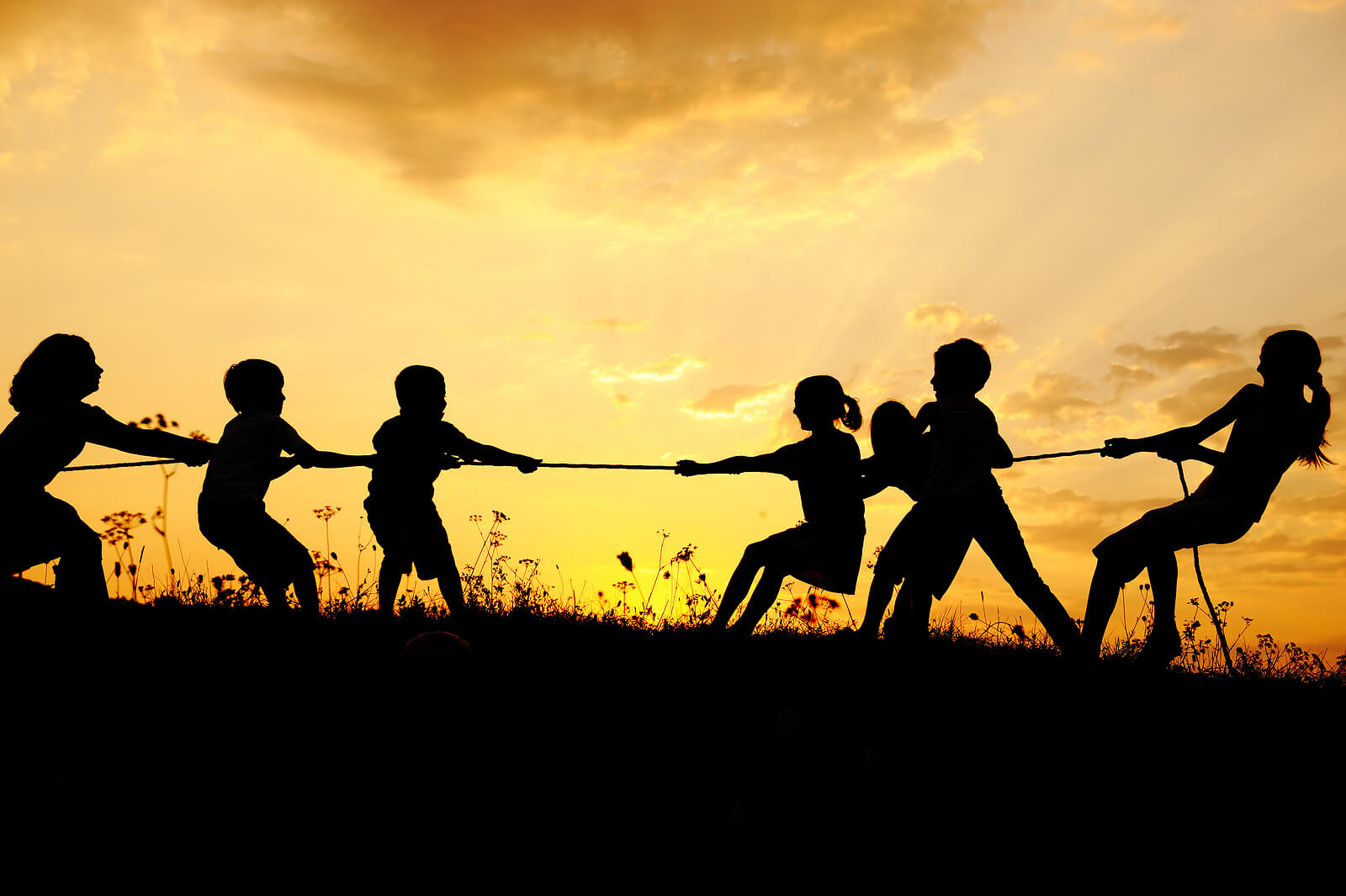 Niños jugando a tirar de la soga al atardecer.