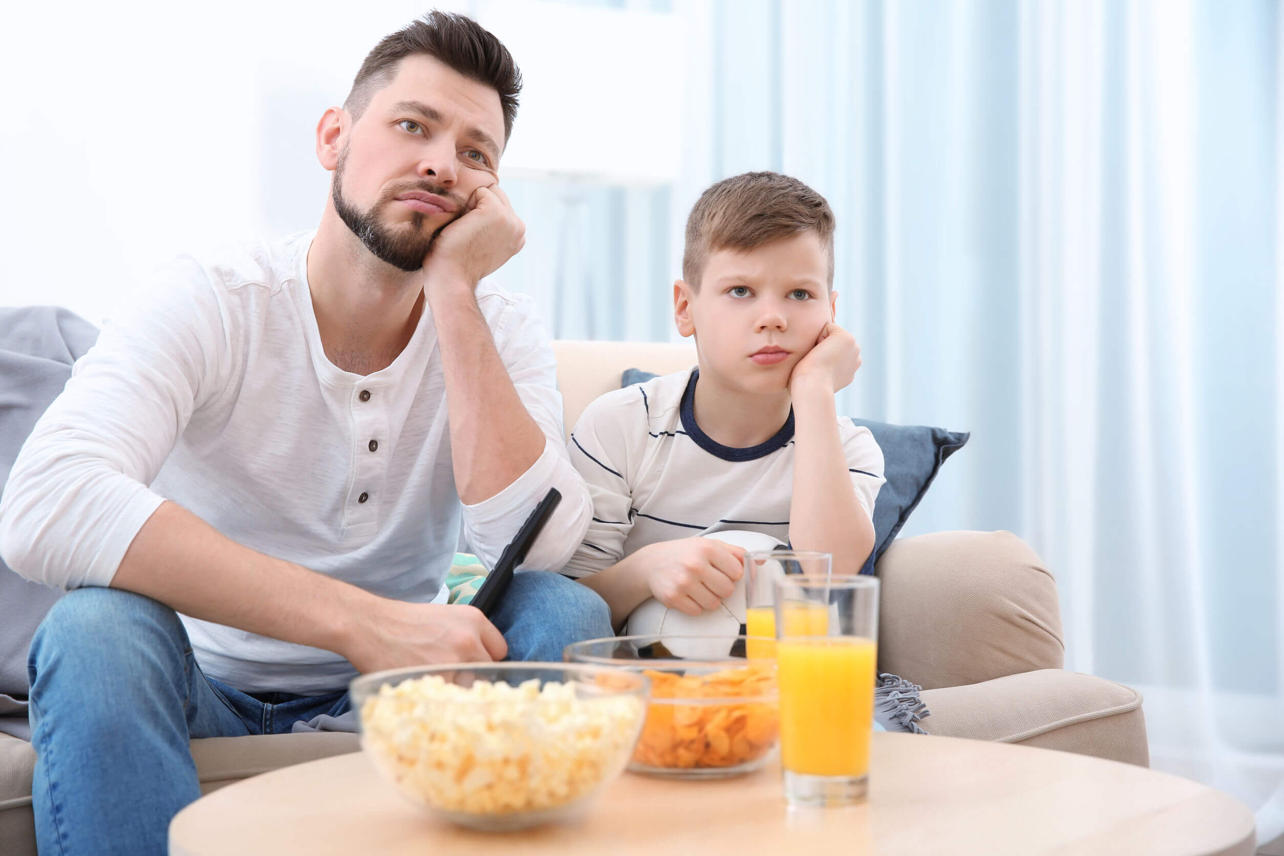 Padre e hijo viendo la televisión mientas comes snaks poco saludables.