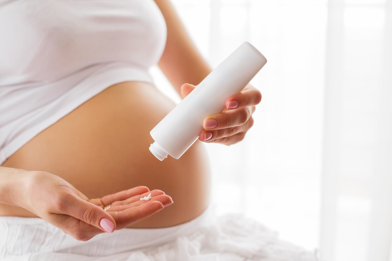A woman applying lotion to her pregnant belly.