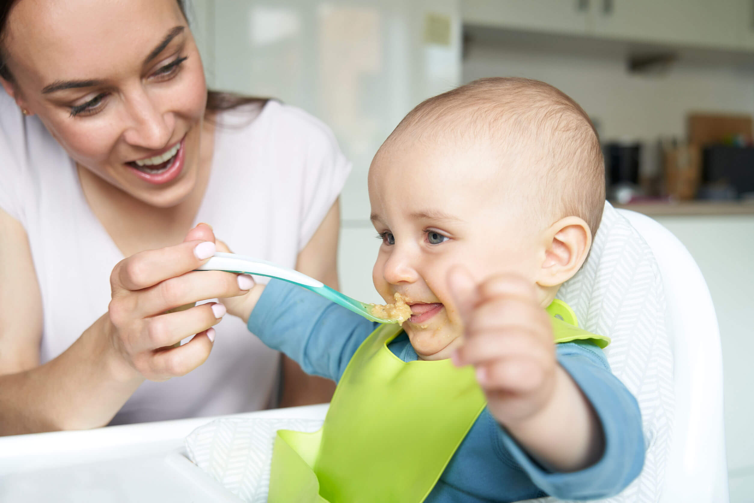 A mother spoon feeding her baby with mashed food.