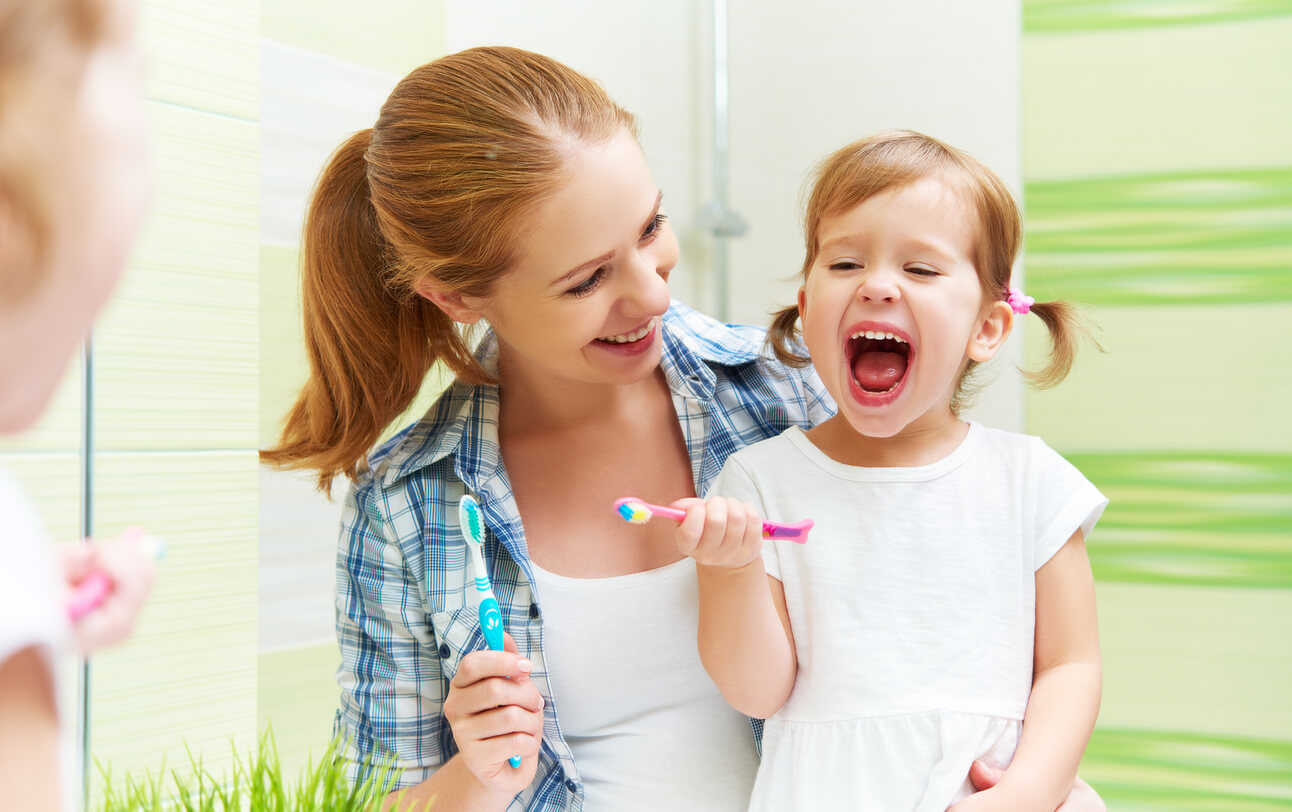 Madre con su hija enseñando a su hijo a cepillarse los dientes y los diferentes cepillos de dientes para niños.