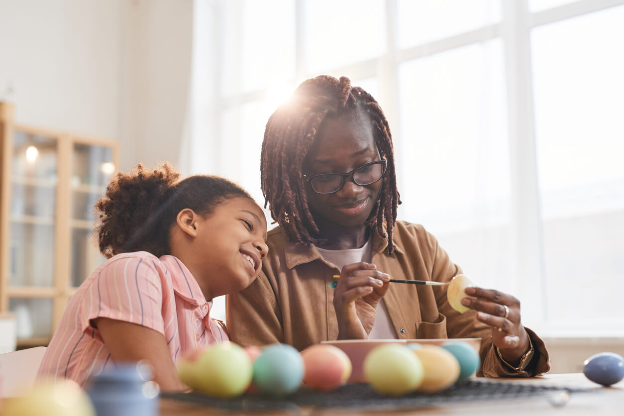 A black mother and daughter decorating Easter eggs together.