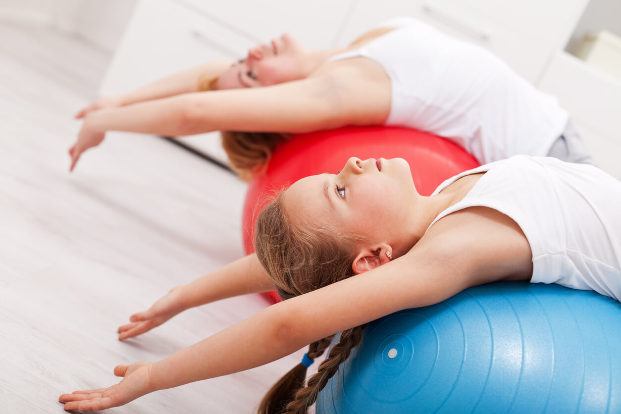 Madre con su hija haciendo ejercicio en casa con la pelota de pilates.