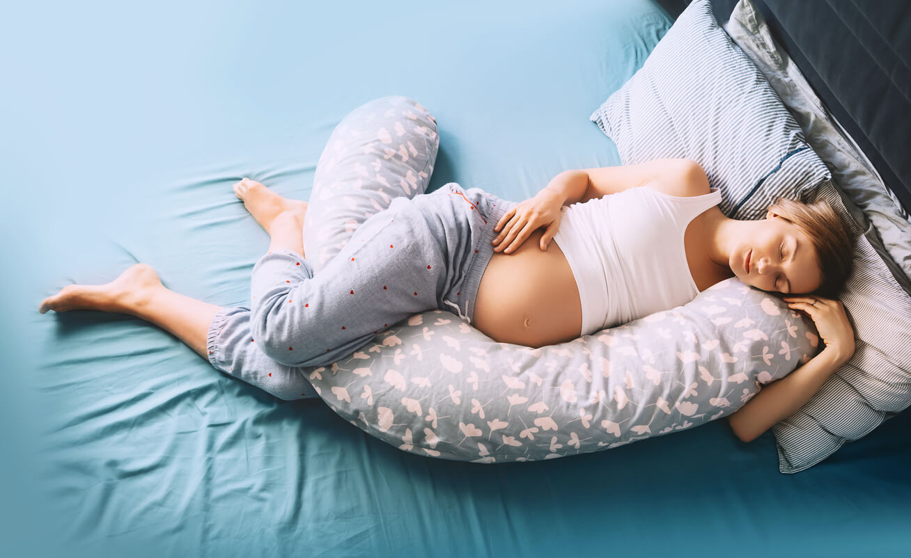 Mulher deitada com um travesseiro de gravidez entre as pernas.