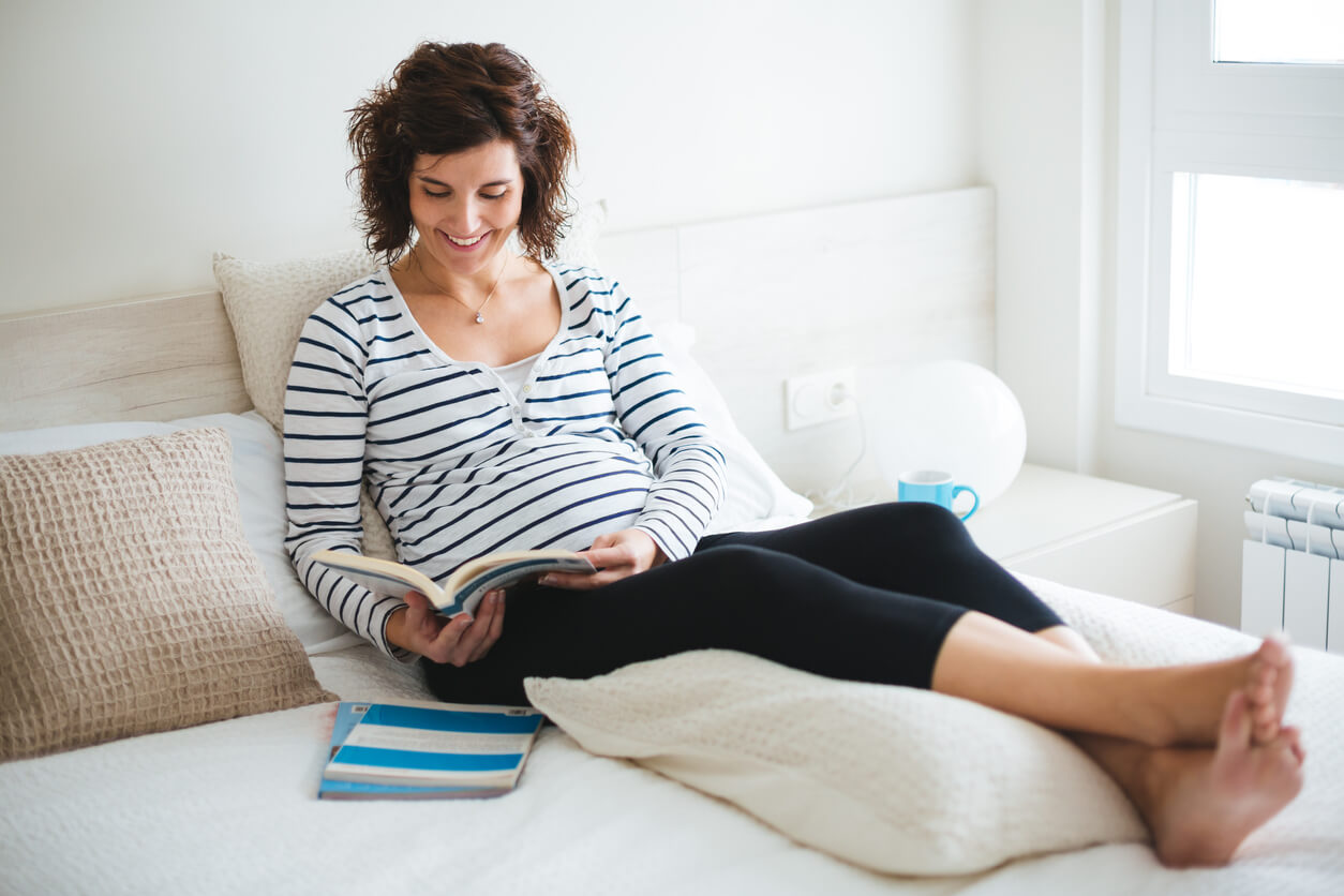 Mujer embarazada leyendo con las piernas en alto.