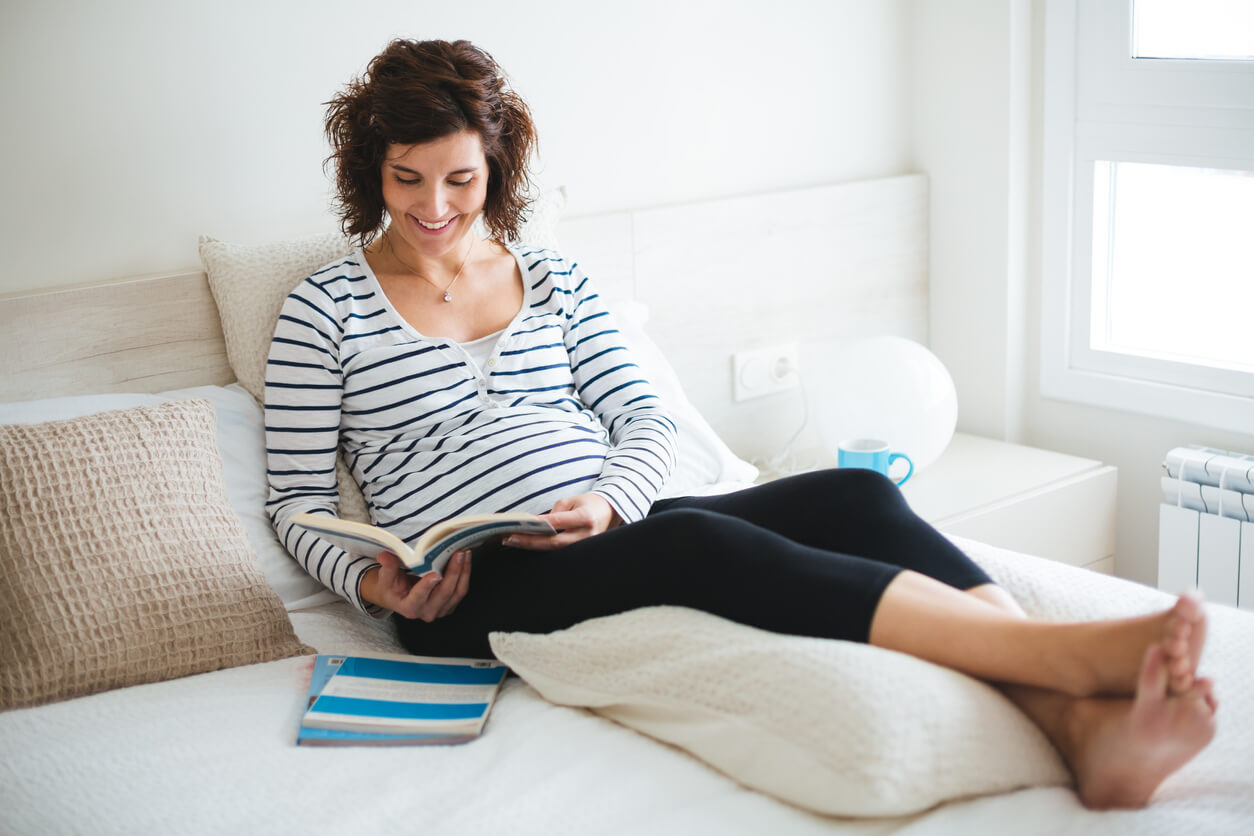 Femme enceinte lisant avec un coussin de grossesse.