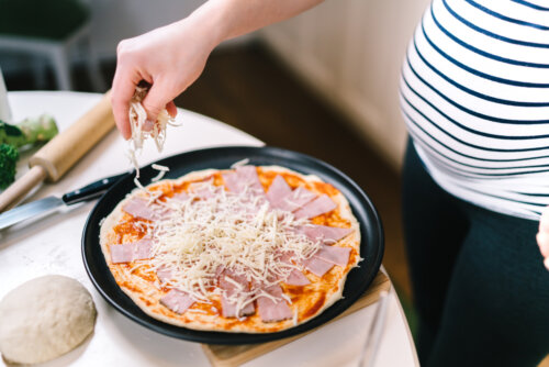 Mujer preparando una pizza con mozzarella durante el embarazo.