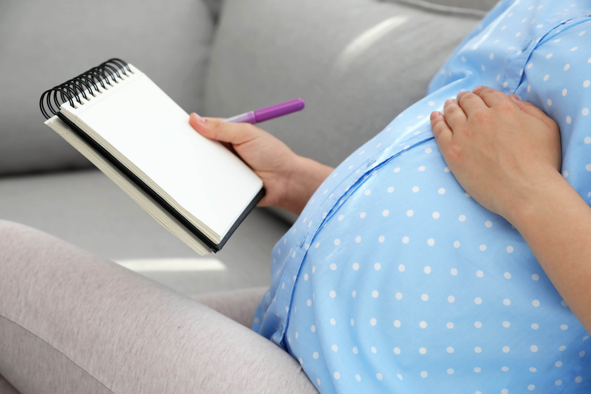 Mujer embarazada pensando y anotando nombres élficos para bebés.