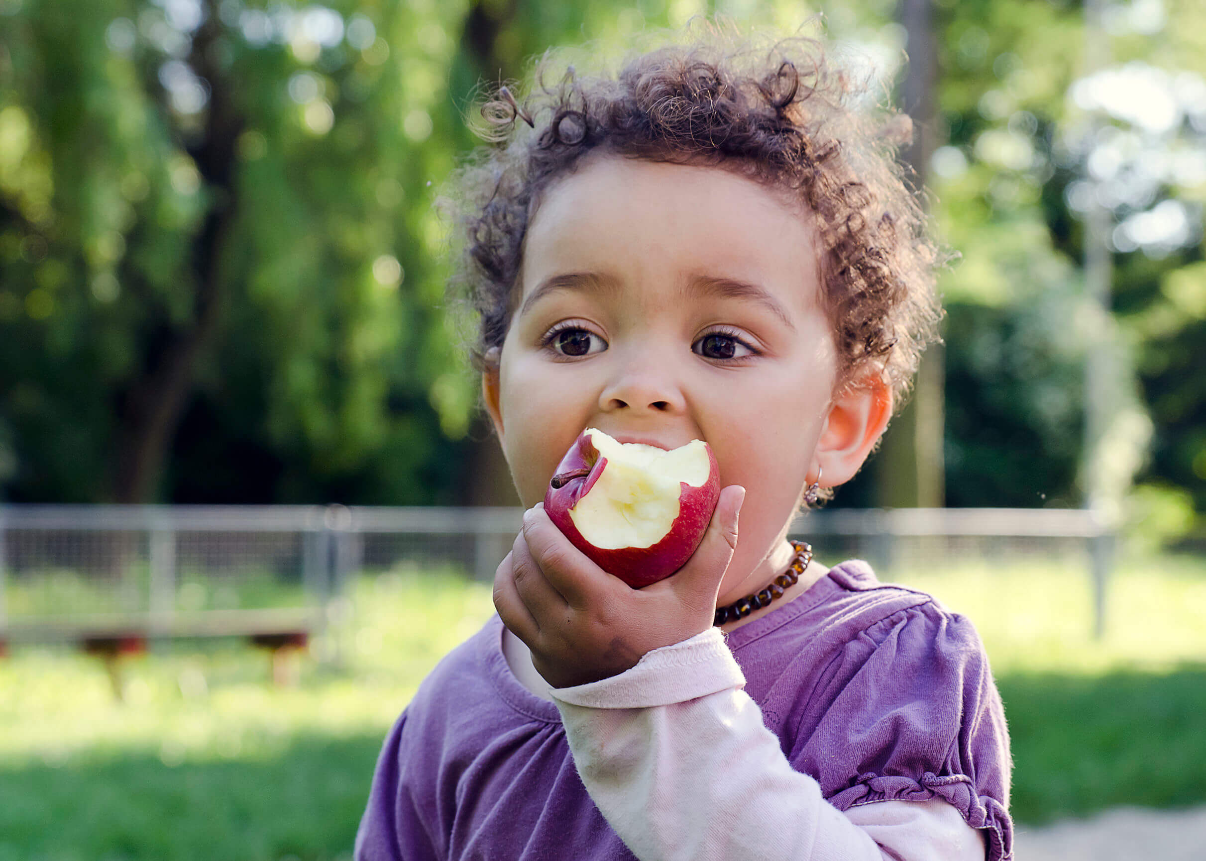 Niña comiendo una manzana como merienda.