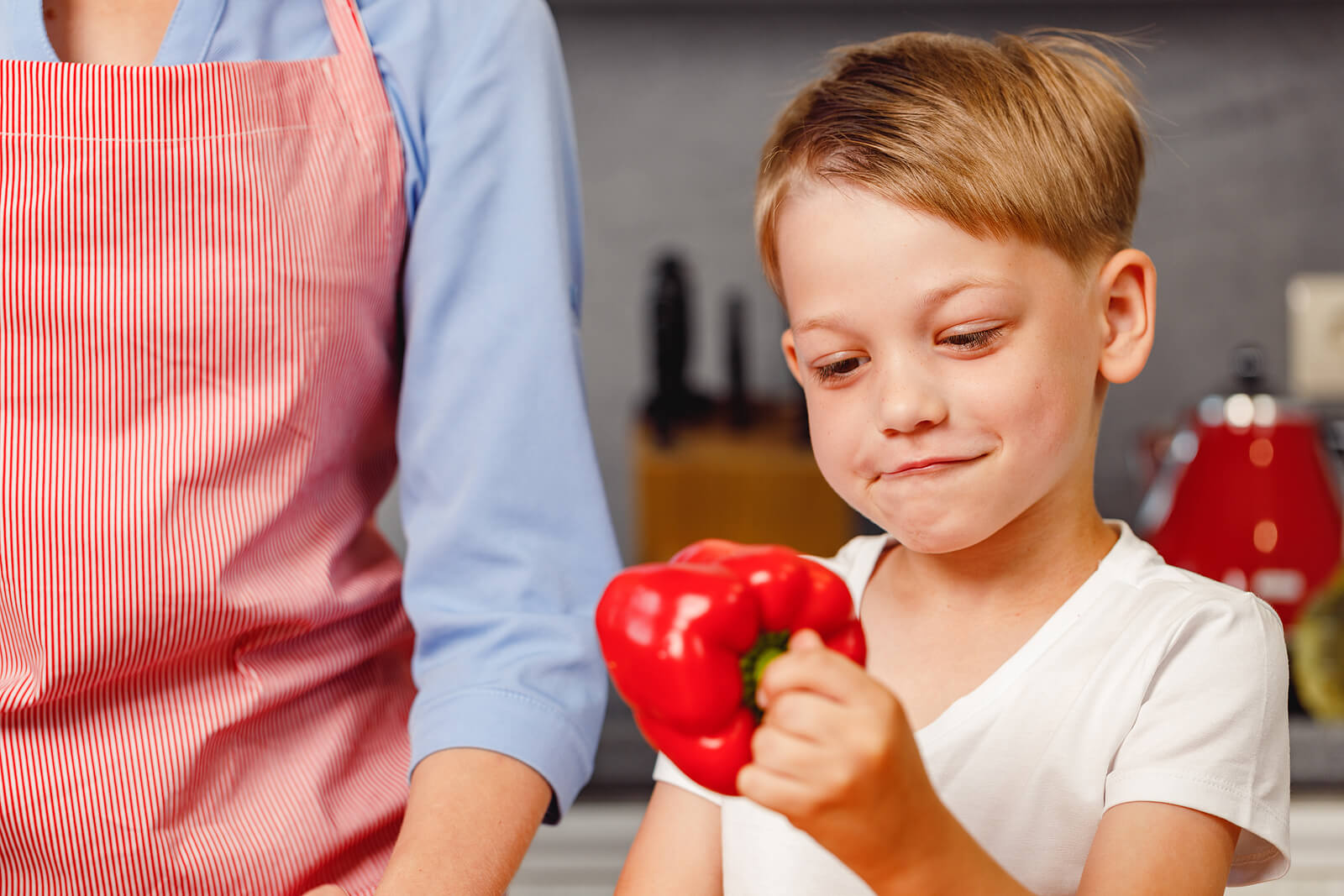 Bambino con un peperone rosso in cucina.