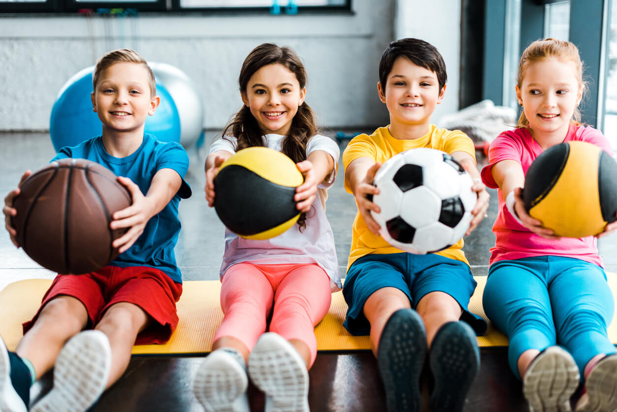Children holding different kinds of sports balls.