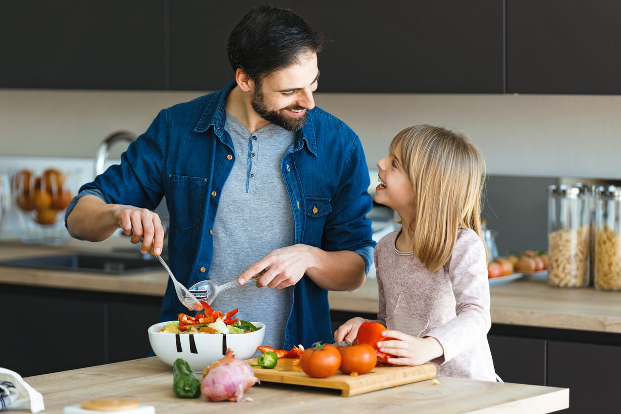Padre e hija cocinando alimentos saludables.