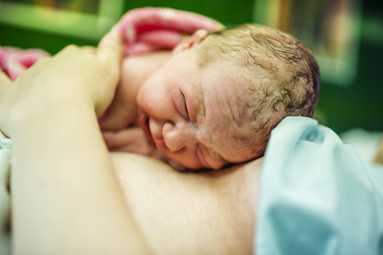 Ett nyfött barn vilar på sin mammas bröst, hud mot hud.