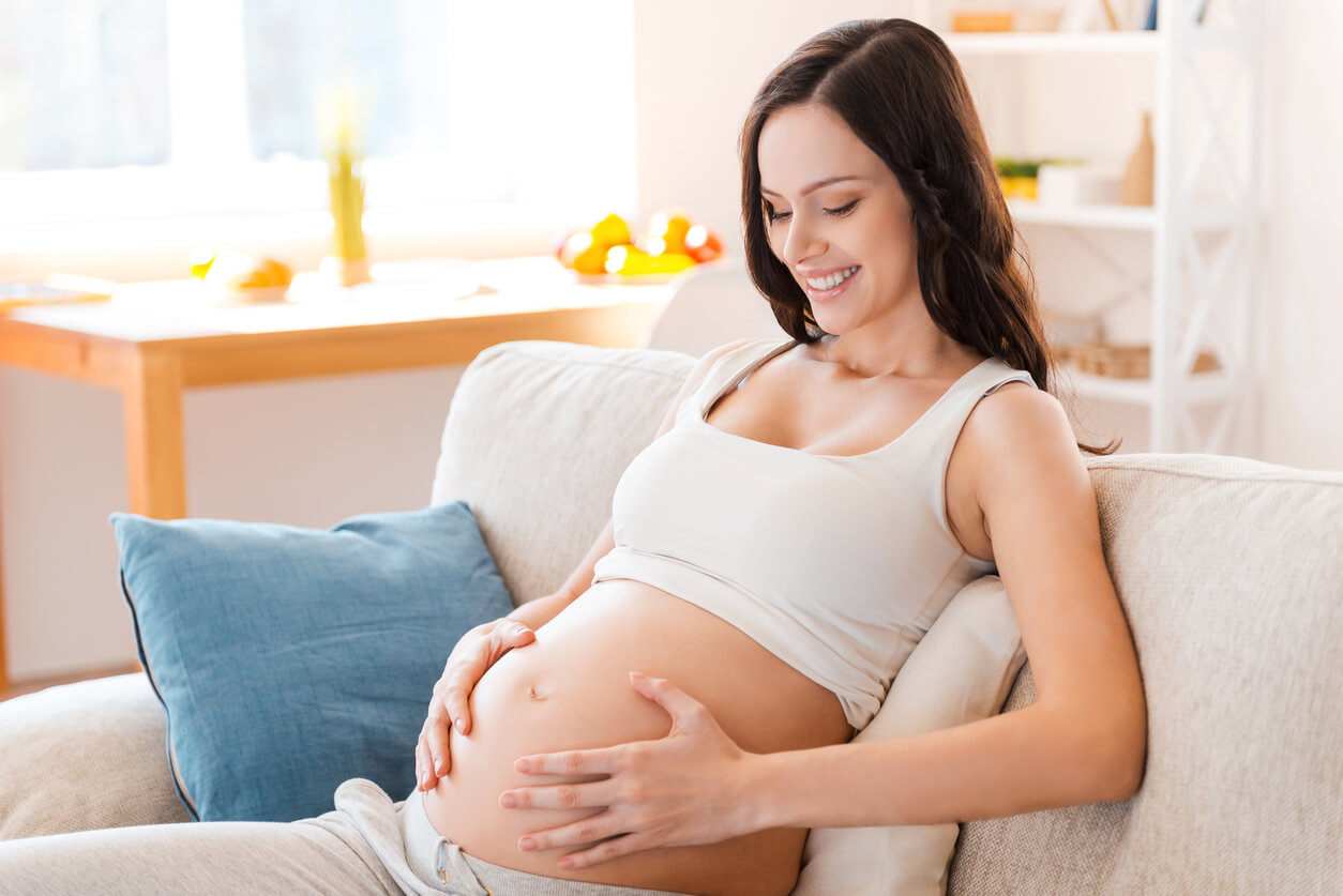 En gravid kvinne smiler ned mot magen hennes.