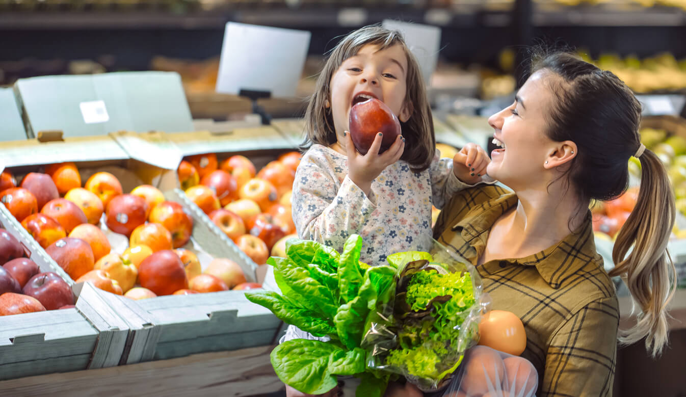 Mère avec sa fille au supermarché au rayon des fruits et légumes.