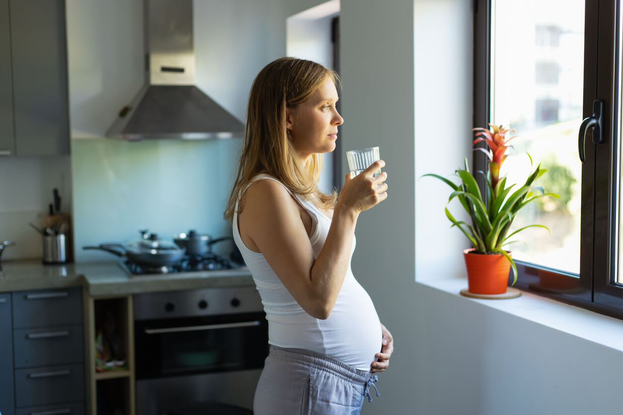 Mujer embarazada bebiendo un vaso de agua para tomarse las vitaminas prenatales.
